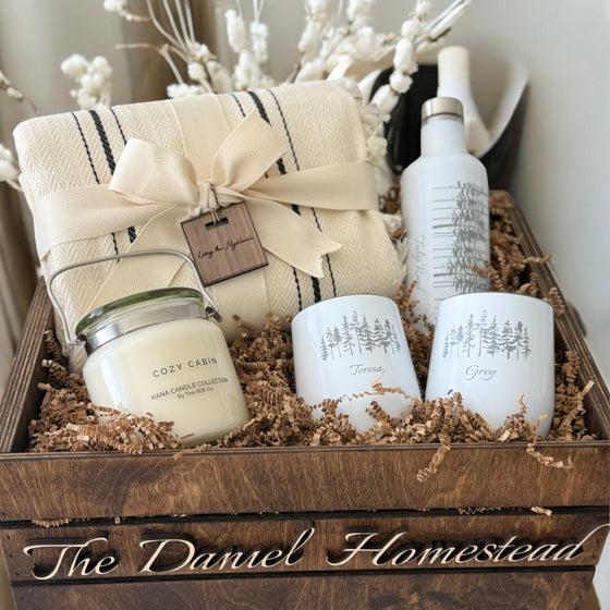 Gift set with candles, tumblers, and a blanket in a wooden crate labeled 'The Daniel Homestead'.