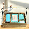 Gift set with teal tumbler, notebook, passport holder, greeting card, luggage tag, and pen in a wooden box.