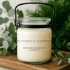Kana Candle in Mahogany & Teakwood, 20oz soy candle in glass jar with handle & Greenery background