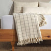 Turkish Throw Blankets in Ivory & Ebony Plaid with tassels neatly folded at the end of  a bed with marching pullows behind 