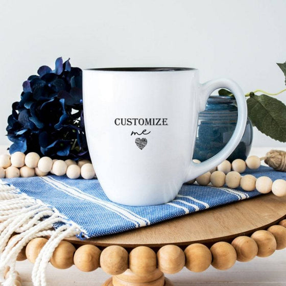 Engraved 16oz white ceramic bistro mug with black interior and custom laser design in black on wood table with blue tablecloth